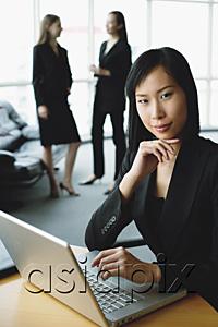 AsiaPix - Businesswoman using laptop, looking at camera, hand on chin