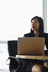 AsiaPix - Businesswoman sitting at desk with laptop, looking away