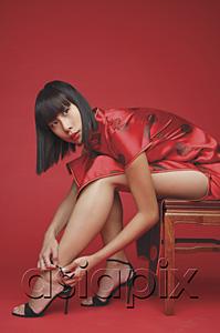 AsiaPix - Woman in cheongsam, bending to adjust strap on shoes