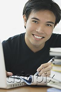 AsiaPix - Young adult smiling at camera, laptop and books next to him
