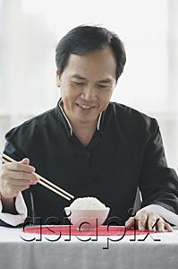 AsiaPix - Man looking at bowl of rice on table, holding chopsticks