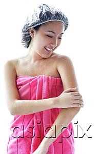 AsiaPix - Young woman wearing shower cap and towel, applying moisturizer to arm