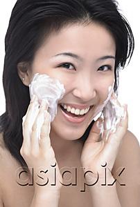 AsiaPix - Young woman putting facial cleanser on her face, looking at camera