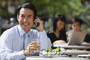AsiaPix - Businessman having lunch at outdoor cafe, using mobile phone, smiling