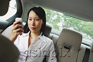 AsiaPix - Businesswoman in backseat of car using mobile phone, text messaging