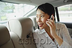 AsiaPix - Businesswoman in backseat of car using mobile phone, smiling