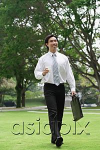 AsiaPix - Businessman carrying briefcase, walking across park
