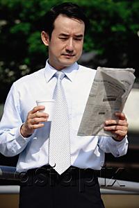 AsiaPix - Businessman looking at newspaper, holding disposable cup