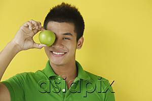 AsiaPix - Man holding green apple over eyes, smiling at camera