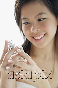 AsiaPix - Young woman looking at perfume bottle, smiling
