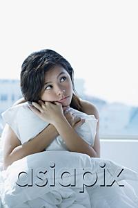 AsiaPix - Young woman on bed, embracing pillow, looking away