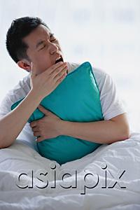 AsiaPix - Man sitting in bed, embracing pillow, yawning