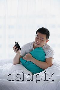 AsiaPix - Man sitting in bed, holding alarm clock