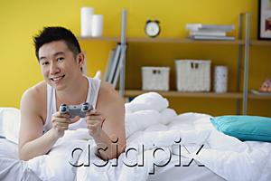 AsiaPix - Man lying on bed, holding video game control