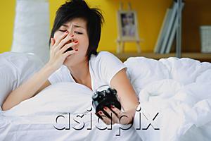 AsiaPix - Woman in bed, looking at alarm clock, yawning