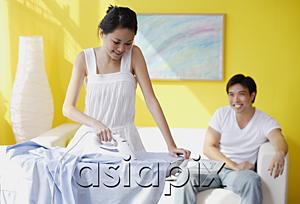 AsiaPix - Couple at home, woman ironing, man sitting on sofa behind her