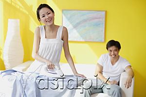 AsiaPix - Couple at home, woman ironing, man sitting on sofa behind her, looking at camera