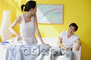 AsiaPix - Couple at home, woman ironing turning to look at man sitting on sofa behind her