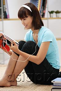 AsiaPix - Young woman looking through magazine, wearing earphones