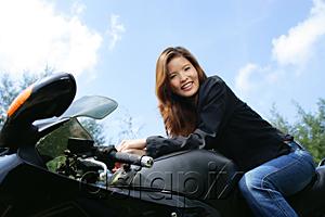 AsiaPix - Young woman sitting on motorcycle, smiling at camera, low angle view