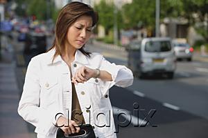 AsiaPix - Woman standing by road, looking at watch