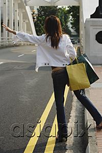 AsiaPix - Woman standing by road, waving for taxi, rear view