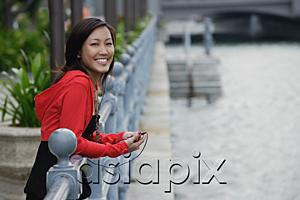 AsiaPix - Woman leaning on railing, listening to MP3 player, smiling at camera