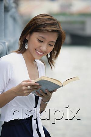 AsiaPix - Woman sitting by river, reading a book