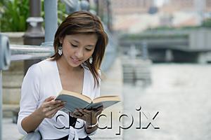 AsiaPix - Woman sitting by river, reading a book