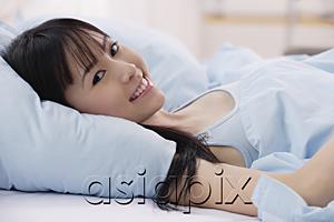 AsiaPix - Young woman lying on bed, smiling at camera