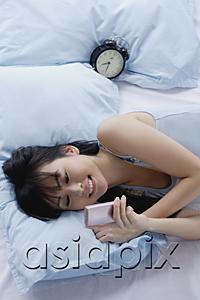 AsiaPix - Young woman lying on bed, looking at mobile phone