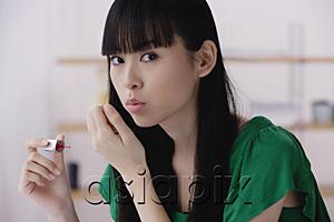 AsiaPix - Young woman applying nail polish, blowing on nails