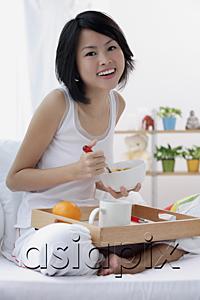 AsiaPix - Young woman having breakfast in bed, smiling at camera