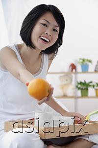 AsiaPix - Young woman holding orange towards camera, smiling