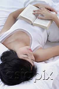 AsiaPix - Young woman sleeping on bed, holding book