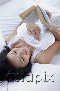 AsiaPix - Young woman on bed, reading a book, high angle view