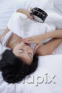 AsiaPix - Young woman on bed, looking at alarm clock, hand on mouth