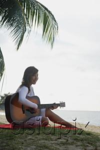 AsiaPix - Young woman sitting on beach playing a guitar