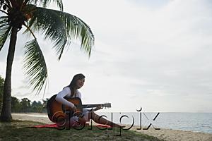 AsiaPix - Young woman sitting on beach with a guitar
