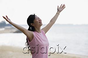 AsiaPix - Woman standing on beach, looking up, arms outstretched