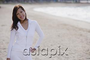 AsiaPix - Young woman standing on beach, hand on hip, smiling at camera