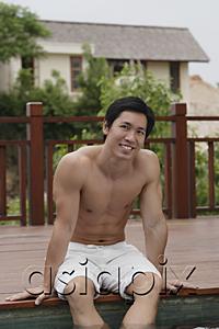 AsiaPix - Man sitting at the edge of swimming pool, smiling at camera
