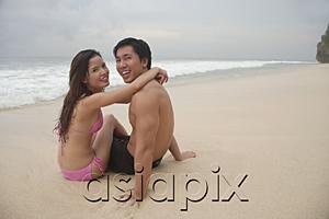 AsiaPix - Couple sitting on beach, embracing, looking at camera
