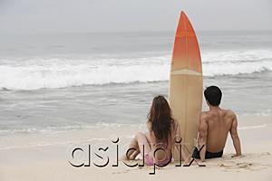 AsiaPix - Couple sitting on beach, surfboard between them, looking out to sea