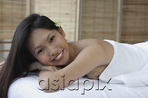 AsiaPix - Young woman lying down on massage table, smiling at camera