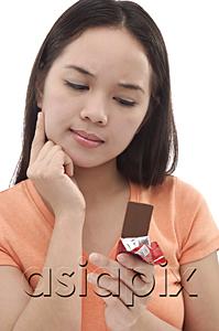 AsiaPix - Young woman looking at a bar of chocolate, hand on chin
