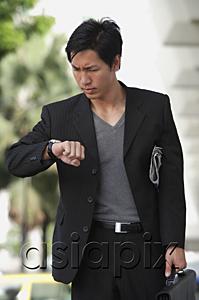 AsiaPix - Businessman holding briefcase, looking at watch, frowning