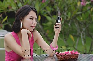 AsiaPix - Young woman sitting at table outdoors, looking at mobile phone