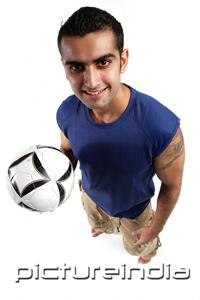 PictureIndia - Young man holding soccer ball in one hand, looking at camera