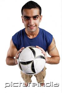 PictureIndia - Young man holding soccer ball, looking at camera